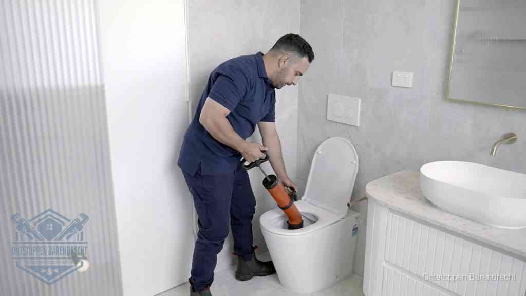 Een monteur buigt over een wandcloset en duwt met de hand een persluchtontstopper in de toiletpot om de verstopping handmatig los te maken in Barendrecht