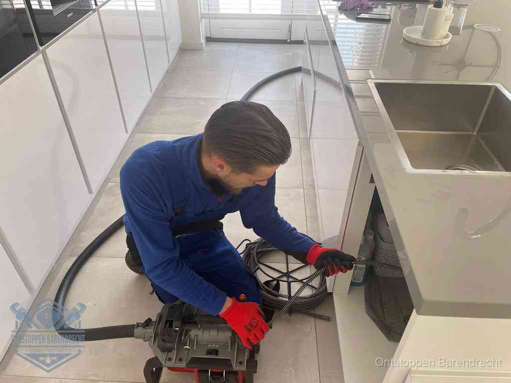 Een monteur ontstopt de keukenafvoer onder de spoelbak met een elektrische veermachine in Barendrecht