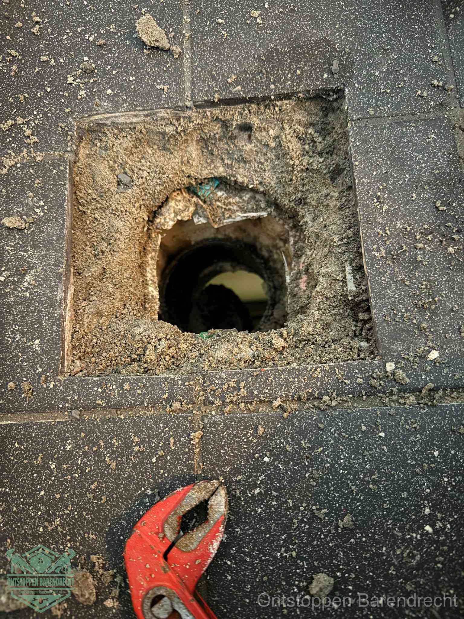 Een geopend rioolputje in een betontegelvloer met losgemaakt rooster en een zichtbare ronde afvoerbuis, het achterhalen waar de afvoerverstopping zit in Barendrecht