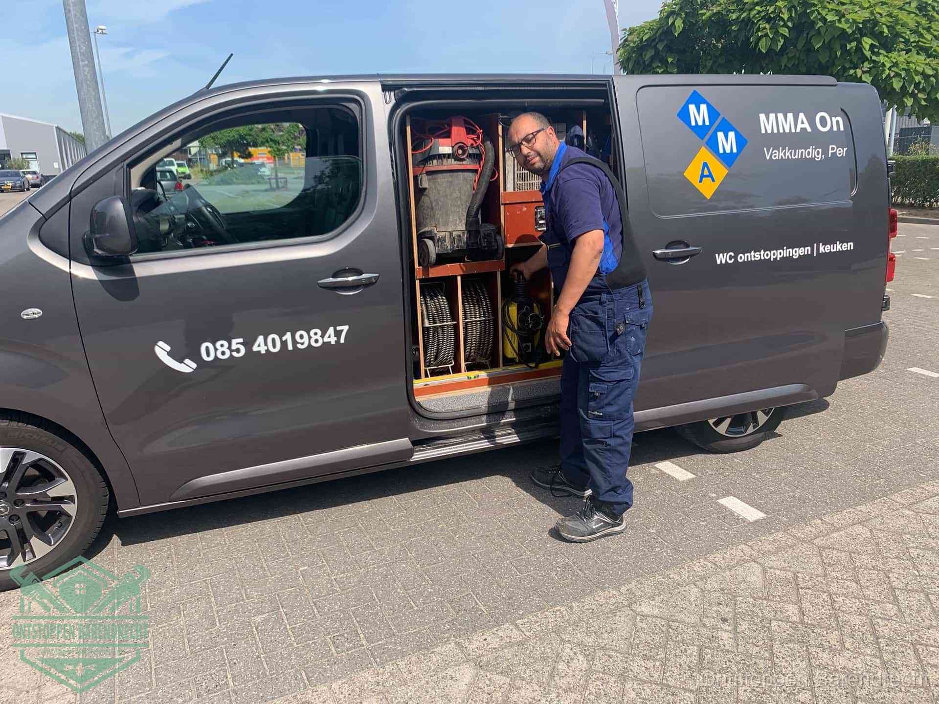 Een monteur bij de open schuifdeur van zijn bedrijfsbus op een parkeerplaats, klaar om de oorzaak van terugkerende afvoerverstoppingen aan te pakken in Barendrecht