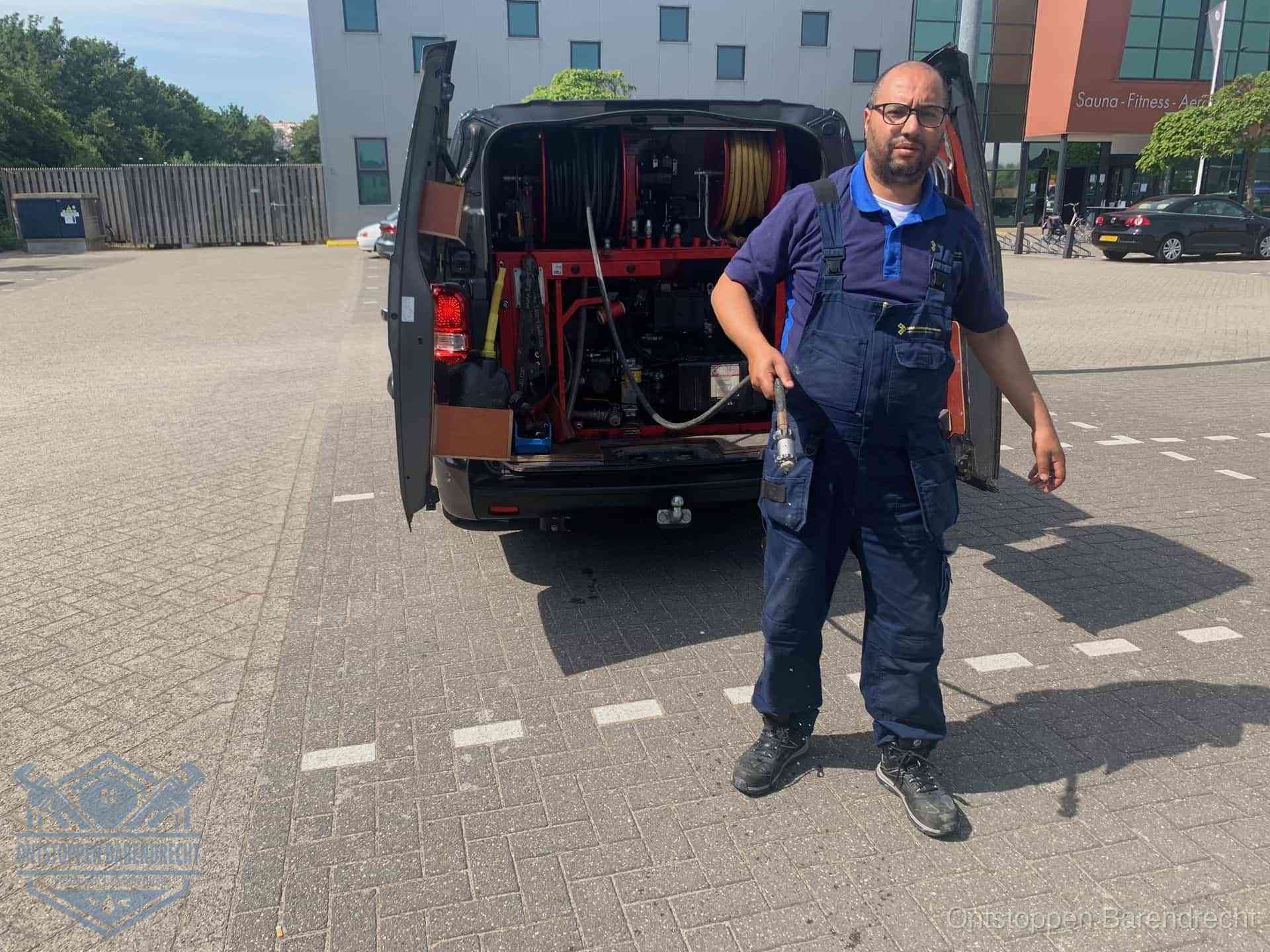 Een monteur bij zijn bestelbus met een hogedruk- en rioolreinigingsunit, klaar om de oorzaak van terugkerende wc-verstoppingen aan te pakken in Barendrecht