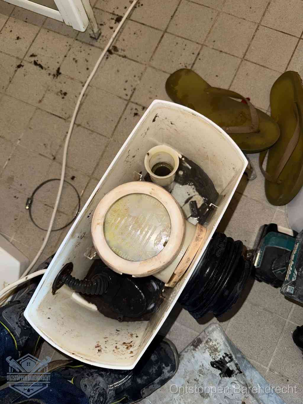 Een gedemonteerde toiletpot op de vloer met ontstoppingsveer en gereedschap ernaast, het verwijderen van een vastzittend voorwerp uit de wc in Barendrecht