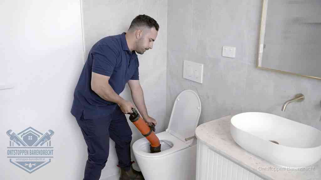 Een man gebruikt een handmatige luchtdruk-ontstopper in een modern betegeld toilet om zelf de wc te ontstoppen in Barendrecht